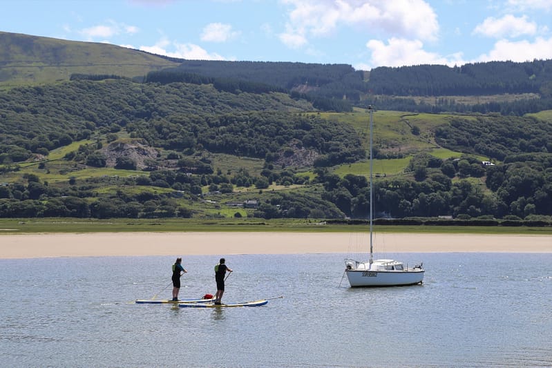 Two people on paddle boards passing a yacht moored in the Mawddach Estuary
