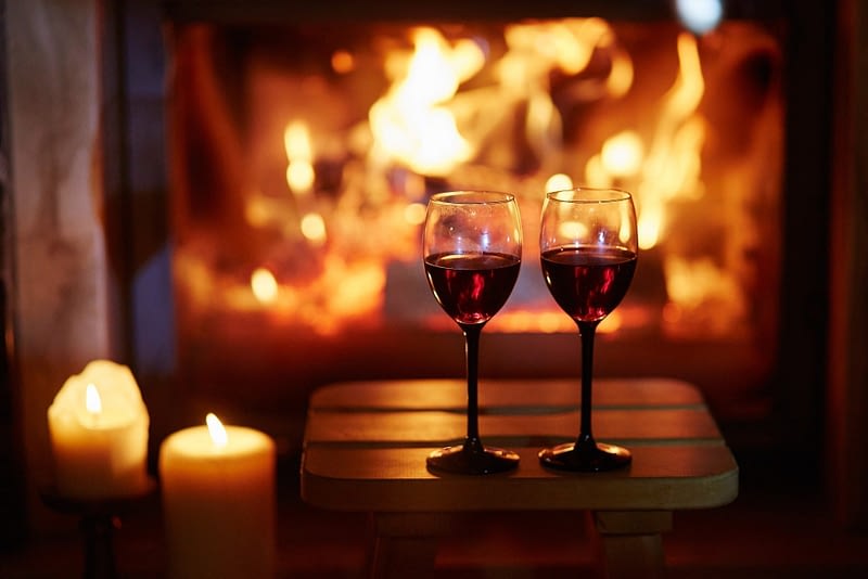 Two glasses of red wine near fireplace with many candles